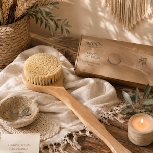 May include: A long-handled wooden dry brush with stiff, light-colored bristles. The brush is accompanied by a brown cardboard box labeled Serenity Wellbeing Tampico Dry Brush Natural Body Care Ritual, featuring a line drawing of the brush.