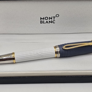 May include: A Montblanc fountain pen featuring a white barrel with vertical ridges and a dark blue cap with horizontal ridges. The pen includes gold-tone accents, a rope-style clip, and a silver-tone tip, presented in a branded display case.