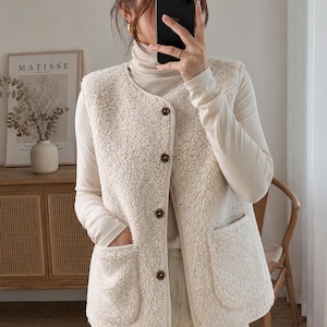 Peut inclure: Un gilet sans manches en sherpa de couleur crème doté d'une encolure en V, d'une fermeture boutonnée à l'avant avec cinq boutons marron foncé et de deux grandes poches plaquées. Le gilet est en matière texturée, type polaire, douce et duveteuse.