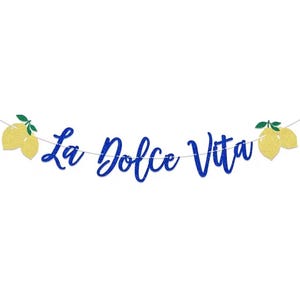 Puede incluir: Una pancarta azul brillante con la frase "La Dolce Vita" en cursiva. La pancarta está ensartada con una fina cuerda blanca y presenta recortes de limones amarillos en cada extremo. Fondo blanco.