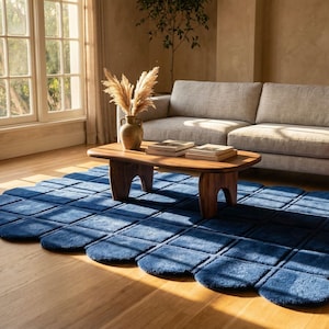 Modern hand tufted blue area rug with a unique scalloped grid design placed in a bright and stylish living room interior. This luxury handmade rug features a plush soft