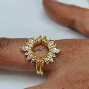 Op de afbeelding: Een goudkleurige open ring met een zonnestraalontwerp versierd met meerdere marquise- en rondgeslepen heldere stenen. Het sieraad toont de tekst Kalikajewelry in het midden. De ringband is gespleten, wat een opening aan de bovenkant creëert.