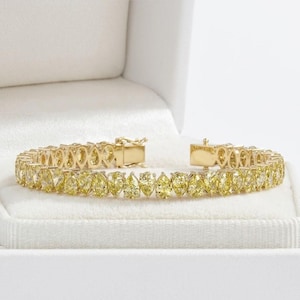 May include: A gold bracelet with yellow gemstones in a pear shape. The bracelet is displayed in a white jewelry box. The gemstones are set closely together, creating a continuous line of sparkle. The clasp is also gold.