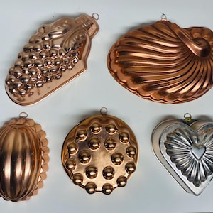 Puede incluir: Cinco moldes antiguos de metal en tonos cobre y plateado de varias formas. Incluye un racimo de uvas, una concha, un óvalo, un círculo con hoyuelos y un corazón. Cada molde tiene un pequeño lazo para colgar. Ideal para hornear o decorar.