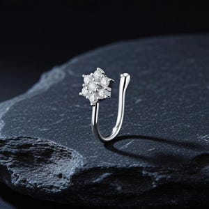 Può includere: Un anello da naso finto color argento con un motivo floreale composto da sette pietre trasparenti a taglio rotondo. Il gioiello presenta una struttura curva a forma di U con un'estremità arrotondata, progettata per aderire alla narice.