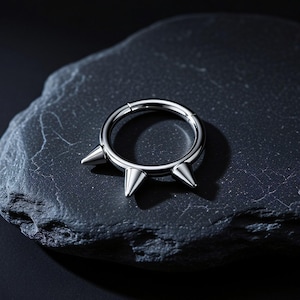 May include: A circular silver-toned metal hoop ring featuring three evenly spaced, pointed conical spikes protruding from the outer edge. The ring has a smooth, polished finish and a hinged segment mechanism for opening and closing the hoop.