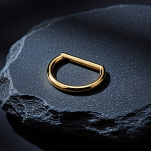 Könnte beinhalten: Ein polierter goldfarbener Metallring in Form des Buchstabens D, bestehend aus einem glatten, abgerundeten halbkreisförmigen Band, das durch einen geraden horizontalen Stab an der Oberseite verbunden ist und eine geometrische Silhouette bildet.