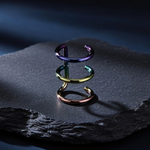 May include: A multi-layered ear cuff featuring a gradient of iridescent colors, transitioning from deep purple at the top to vibrant green in the middle and a warm copper tone at the base, constructed from three thin, polished metal bands.