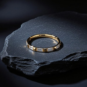 May include: A gold ring with rectangular, clear gemstones set in a repeating pattern. The ring is on a dark, textured surface, with the gold band and gemstones catching the light. The ring is a piece of jewelry.