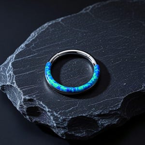 May include: A circular hinged segment ring featuring a polished metallic finish on one half and a vibrant, mottled inlay of blue and green tones on the other half. The jewelry piece is designed with a seamless closure mechanism for a smooth appearance.