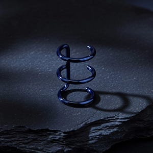 May include: A dark blue, spiral-shaped metal object with three curved rings connected by a central vertical bar. The object is set against a dark, textured background, creating a contrast that highlights its form and colour.