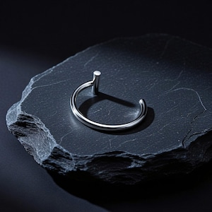 May include: A polished silver-tone metal hoop earring featuring a smooth, circular band with a single vertical cylindrical post attached at one end. The jewellery piece has a reflective, metallic finish and a simple, open-ended design structure.