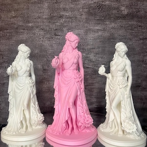 Three Persephone statues displayed together, featuring two elegant white Greek goddess sculptures and one pink centerpiece. Inspired by Greek mythology, Persephone, Queen of the Underworld, holds a symbolic pomegranate while wearing flowing drapery decorated with detailed roses. This comparison photo showcases available color options and handcrafted 3D printed details, perfect for altar decor, pagan decor, mythology collections, witchcraft spaces, and feminine home decor.