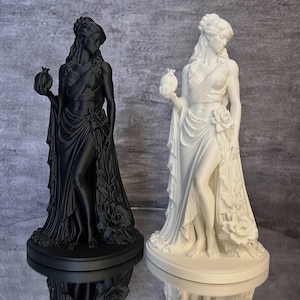 Black and white Persephone Statue displayed side by side to compare available color options. This detailed Greek Goddess sculpture features a symbolic pomegranate, flowing classical robes, and floral accents inspired by Greek mythology. Perfect for pagan altar decor, witchcraft decor, mythology collections, gothic home decor, and lovers of ancient Greek goddesses.
