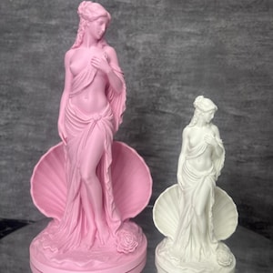 Op de afbeelding: Twee beelden van een figuur in een schelp, &eacute;&eacute;n roze en &eacute;&eacute;n wit. Het roze beeld is 23 cm hoog en het witte beeld is 15 cm hoog. Beide figuren hebben gedrapeerde stof, gedetailleerd haar en een roos aan de basis van de schelp.