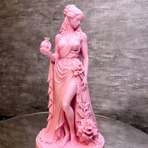 Pink Persephone Statue displayed in natural daylight, featuring the Greek Goddess holding a detailed pomegranate and wearing flowing robes decorated with elegant roses. This handcrafted Greek mythology sculpture is ideal for pagan altar decor, witchcraft decor, gothic home decor, mythology collections, spiritual spaces, and unique fantasy-inspired gifts.