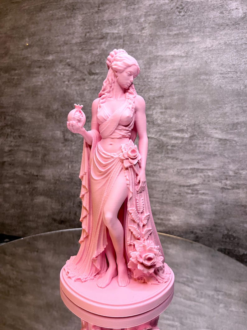 Pink Persephone Statue displayed in natural daylight, featuring the Greek Goddess holding a detailed pomegranate and wearing flowing robes decorated with elegant roses. This handcrafted Greek mythology sculpture is ideal for pagan altar decor, witchcraft decor, gothic home decor, mythology collections, spiritual spaces, and unique fantasy-inspired gifts.