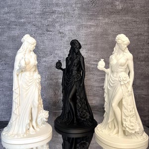Three Persephone Statue color display featuring a matte black sculpture surrounded by two white versions, showcasing available finishes and size options. This elegant Greek Goddess figurine with a symbolic pomegranate and detailed floral design is inspired by Greek mythology and makes a beautiful pagan altar decoration, mythology collectible, gothic home decor piece, or meaningful gift.