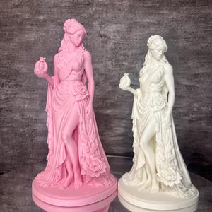 Two Persephone statues shown side by side in pink and white PLA, highlighting the elegant design inspired by Greek mythology. The Goddess of Spring and Queen of the Underworld is depicted holding a symbolic pomegranate with flowing robes and blooming roses, representing rebirth, abundance, and transformation. This comparison image displays available color choices for mythology lovers, pagan altar decor, witchcraft decor, spiritual gifts, and aesthetic home decoration.