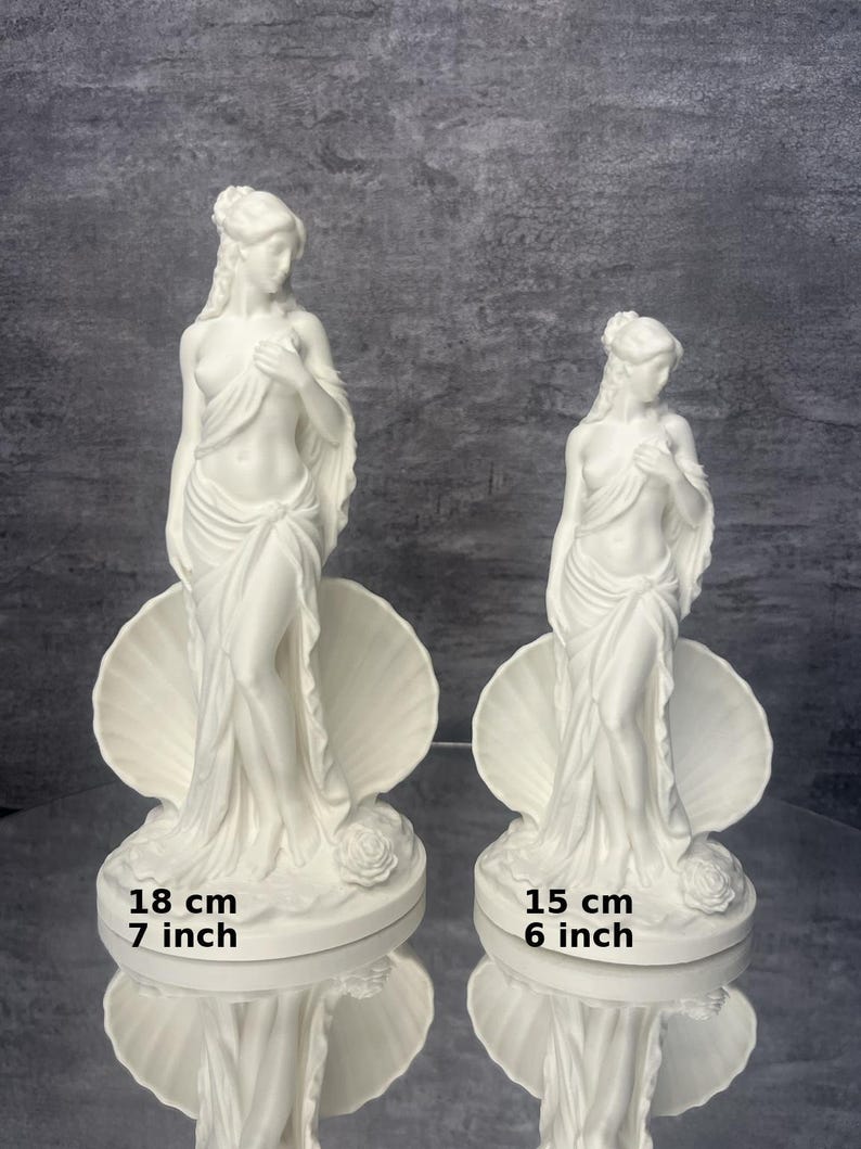 Op de afbeelding: Twee witte beelden van een staande figuur gedrapeerd in stof, geplaatst voor een grote schelp. Het grotere beeld meet 18 cm en het kleinere beeld meet 15 cm. Beide figuren zijn voorzien van een roos aan de basis van het beeldhouwwerk.
