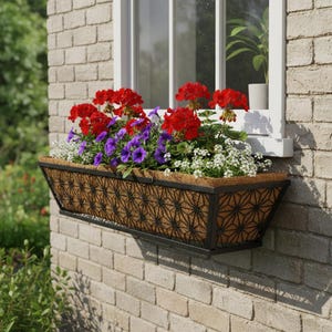 Puede incluir: Una jardinera rectangular llena de geranios rojos vibrantes, petunias moradas y flores blancas. La jardinera tiene un marco de metal negro con un diseño geométrico y está montada en una pared de ladrillo.
