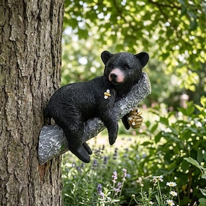 Peut inclure: Sculpture d'un ourson noir se reposant sur une branche d'arbre, avec un petit nid d'abeilles. L'ours a un nez rose et est fixé à un tronc d'arbre. La sculpture est conçue pour l'extérieur et ajoute une touche fantaisiste à tout jardin.