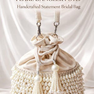 May include: A cream-colored bridal bag with pearl embellishments. The bag features a drawstring closure, pearl tassels, and a beaded fringe. The text "LUXE NUDE PEARL DANGLER POTLI Handcrafted Statement Bridal Bag" is displayed.