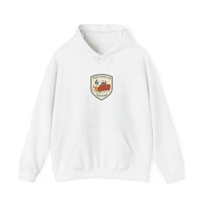 Peut inclure: Sweat à capuche blanc avec une poche avant et un cordon de serrage. Le sweat-shirt présente un motif sur la poitrine avec le texte "Drought National Park" et une illustration d'un canapé et d'une plante.