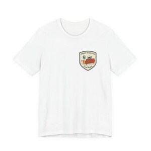 May include: White t-shirt featuring a shield-shaped graphic. The graphic includes a couch, plant, and text: "Yosemite National Park" and "Couch Patrol". A casual, everyday wear item.