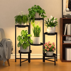 May include: A black metal multi-tiered plant stand featuring six circular shelves arranged at varying heights. Three of the shelves are equipped with integrated circular LED grow lights that illuminate the potted plants placed directly above them.