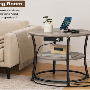 May include: A gray and black round side table with two shelves. The top shelf holds a phone charging stand with a phone, a small plant, and a watch. The table has built-in outlets and a power cord. The text "Living Room" and "Keep your devices charged and your space organized" are visible.