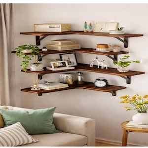 May include: A corner wall shelf unit with four dark brown wooden shelves supported by black metal brackets. The shelves are decorated with plants, books, and decorative items. The shelves are mounted on a white wall.