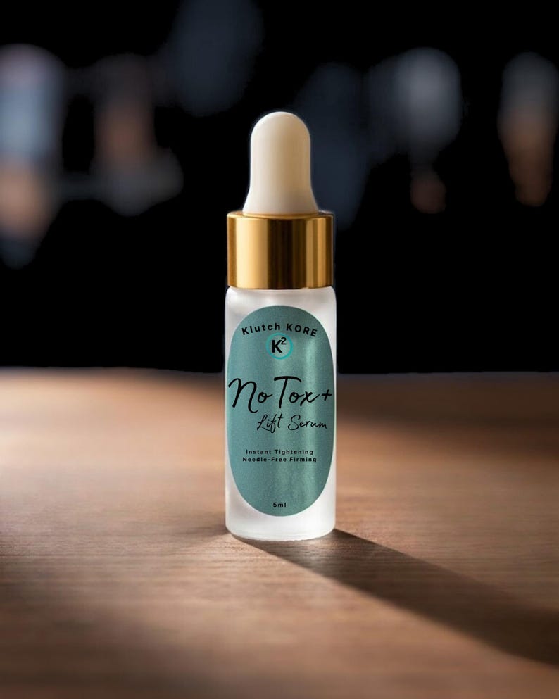 May include: A small, frosted glass bottle with a white dropper and gold-colored cap. The label reads "Klutch Kore K2 No Tox+ Lift Serum" with text below indicating instant tightening and needle-free firming. The bottle is 5ml.