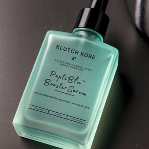 Puede incluir: Una botella cuadrada turquesa de PeptiBlu Booster Serum de Klutch Kore. La botella tiene un cuentagotas negro y texto blanco que dice "Clinician Formulated Hand Crafted". Los ingredientes incluyen GHK-CU Copper Peptide, Blue Tansy y &Aacute;cido Hialur&oacute;nico.