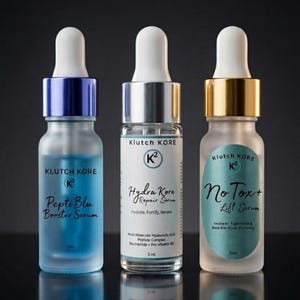 May include: Three glass serum bottles with white droppers. The bottles have blue, silver, and gold accents. Each bottle has the "Klutch Kore" logo and product names: "Pepti Blu Booster Serum", "Hydra Kore Repair Serum", and "No Tox+ Lift Serum".