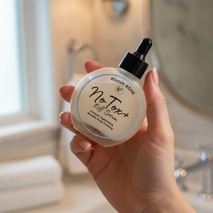 May include: A round, clear bottle of NoTox+ Lift Serum is held in a hand. The bottle has a black dropper and a white label with blue text. The label includes the words "Instant Tightening" and "Needle-Free Firming". The bottle contains 2 oz/60ml.