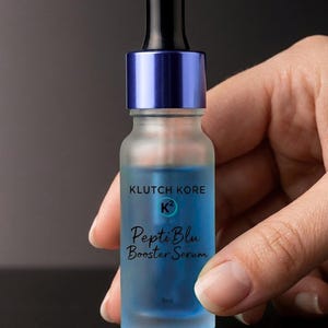May include: A frosted glass bottle of PeptiBlu Booster Serum with a blue liquid inside. The bottle has a blue cap and a black dropper. The text "KLUTCH KORE" and "PeptiBlu Booster Serum" are printed on the bottle. The bottom of the bottle reads "Firming + Barrier Repair".