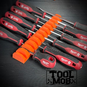 May include: A collection of black and red screwdrivers with silver shafts, arranged in an orange holder. The screwdrivers are labeled "Milwaukee" and are set against a black, textured surface. The text "TOOL MOBX" is visible.