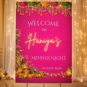 May include: A magenta sign on a stand with the words "WELCOME to Haniya's MEHNDI NIGHT" in white and gold lettering. The date "23. NOV, 2026" is at the bottom. The sign is decorated with floral arrangements and hanging ornaments.