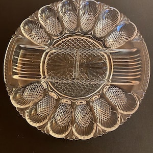 May include: Clear glass serving dish with multiple compartments. The dish has a round shape with a central section and surrounding sections, each with a textured pattern. The dish is designed for serving appetizers or snacks.