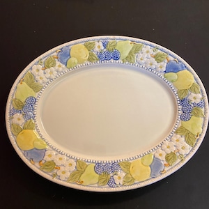 May include: An oval serving platter with a white center and a decorative border. The border features embossed images of pears, blueberries, and white flowers in shades of yellow, green, and blue. The platter measures approximately 12 inches in length.