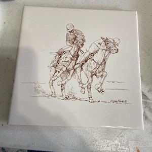 May include: Square white ceramic tile featuring a sepia-toned illustration of two horses and riders in a polo match. The artwork includes fine details of the horses' musculature and the riders' attire. Signed by Anna Phok.