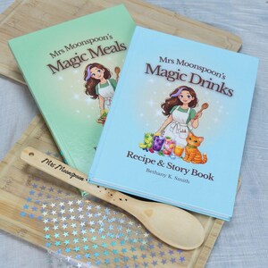 Puede incluir: Se muestran dos libros de recetas e historias titulados "Mrs Moonspoon's Magic Meals" y "Mrs Moonspoon's Magic Drinks". También hay una cuchara de madera con el texto "Mrs Moonspoon". Los libros presentan ilustraciones de una mujer y un gato.