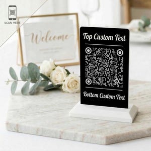 May include: A white ceramic mug with a black handle and the text "But first, coffee" in a black, handwritten-style font. The mug is on a white surface.