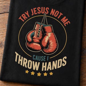 Puede incluir: Camiseta negra con un gráfico de guantes de boxeo rojos dentro de un círculo. El texto dice "Try Jesus Not Me Cause I Throw Hands" en un estilo vintage. Cinco estrellas doradas están debajo.