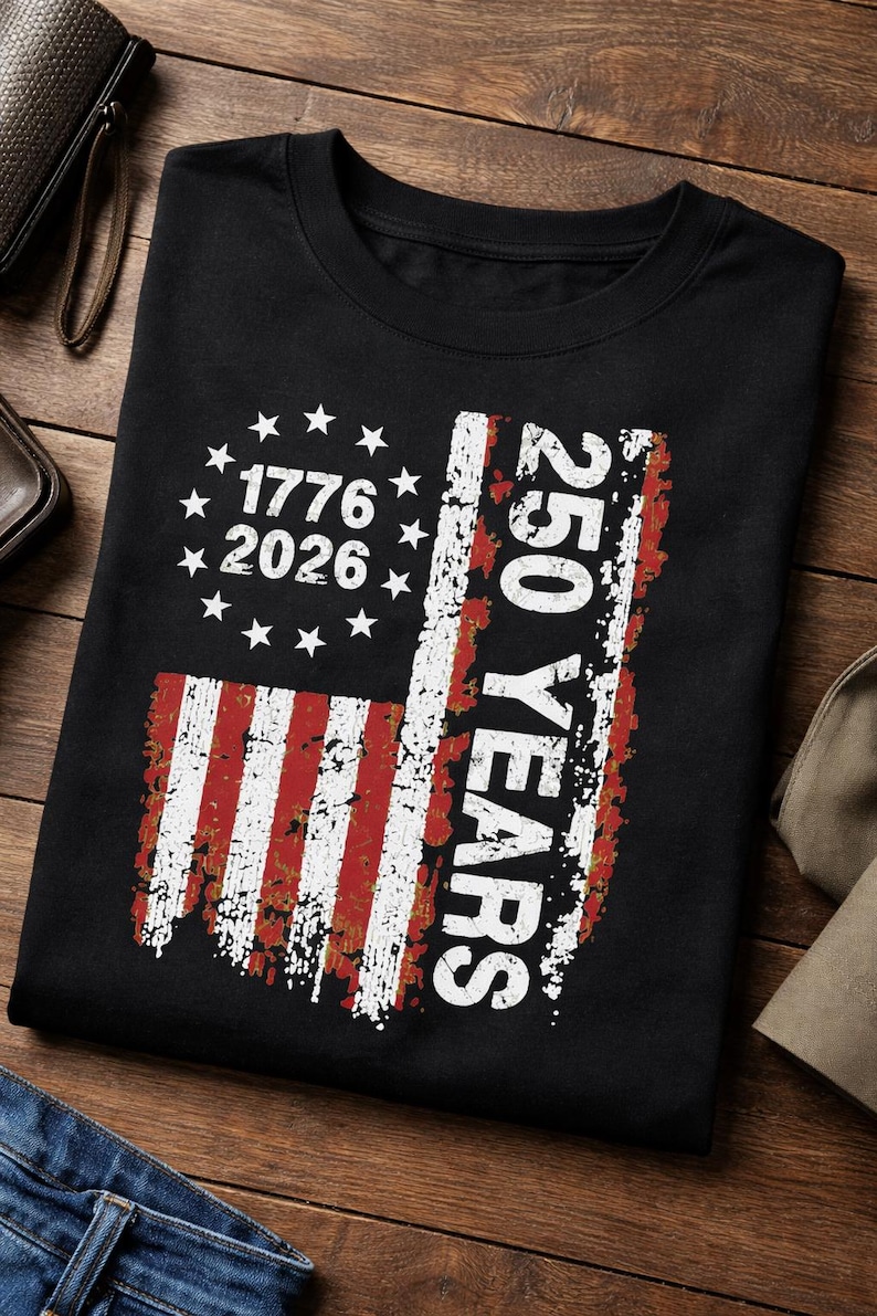 Pu&ograve; includere: T-shirt nera con un design invecchiato della bandiera americana. Il design include il testo "1776 2026" e "250 YEARS". La bandiera presenta strisce rosse e bianche e stelle bianche, celebrando un anniversario significativo.