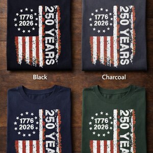 Pu&ograve; includere: Quattro magliette in nero, antracite, blu navy e verde scuro, ciascuna con un design a bandiera americana invecchiata. Le magliette mostrano il testo "1776 2026" e "250 YEARS". La frase "Best Colors For Printing" &egrave; in alto.