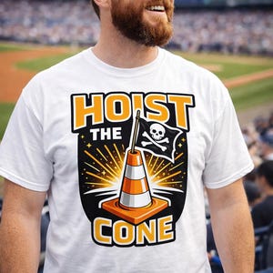 Puede incluir: Camiseta blanca con el texto "HOIST THE CONE" en naranja y negro. El dise&ntilde;o presenta un cono de tr&aacute;fico con una bandera pirata. La persona de la imagen lleva una gorra de b&eacute;isbol azul marino.