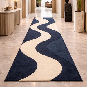May include: A navy blue and cream-colored runner rug with a wavy design. The rug is rectangular and features a central cream-colored wave pattern against a navy blue background. The rug is placed in a hallway.