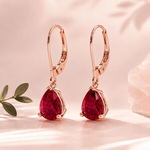 Peut inclure: Une paire de boucles d'oreilles à fermoir levier en or rose avec des pierres rouge foncé taillées en forme de poire. Le métal présente une finition métallique chaude et les pierres sont fixées par de petites griffes à la base de chaque boucle.
